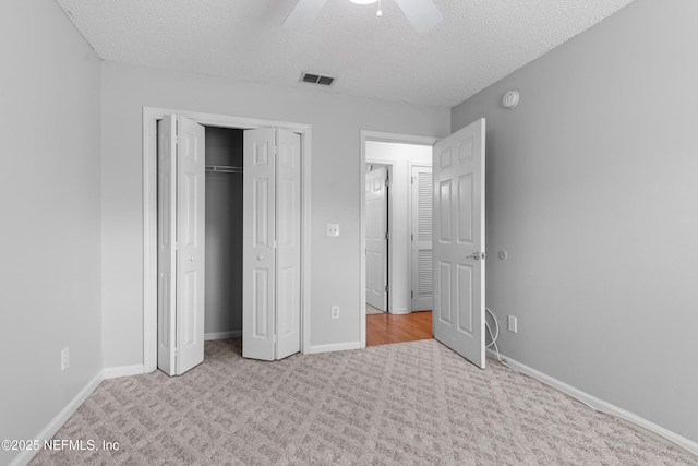 unfurnished bedroom with ceiling fan, light colored carpet, a textured ceiling, and a closet