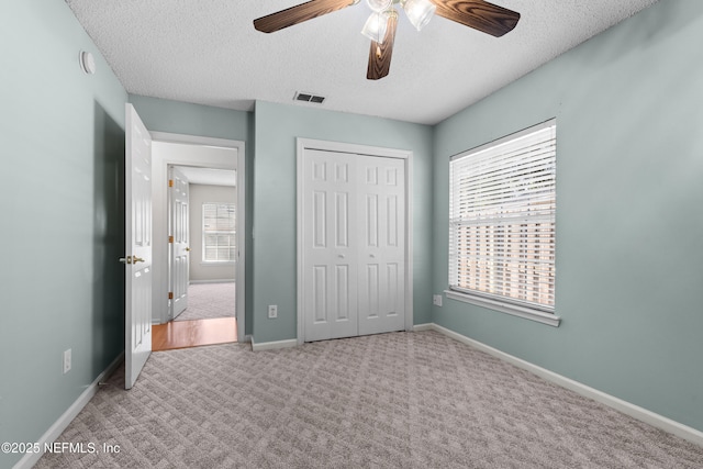 unfurnished bedroom with ceiling fan, light colored carpet, a closet, and a textured ceiling