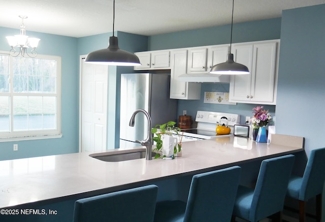 kitchen with sink, white range with electric stovetop, pendant lighting, white cabinets, and stainless steel refrigerator