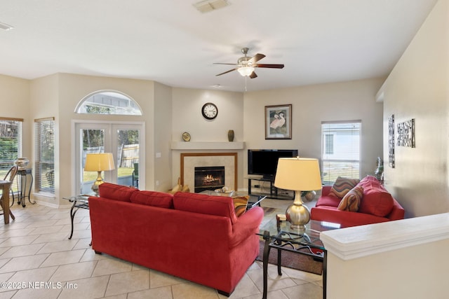 tiled living room with a tiled fireplace, french doors, and ceiling fan