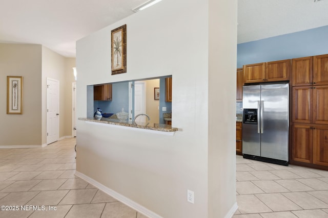 kitchen featuring light tile patterned floors, sink, stainless steel fridge, a towering ceiling, and light stone counters