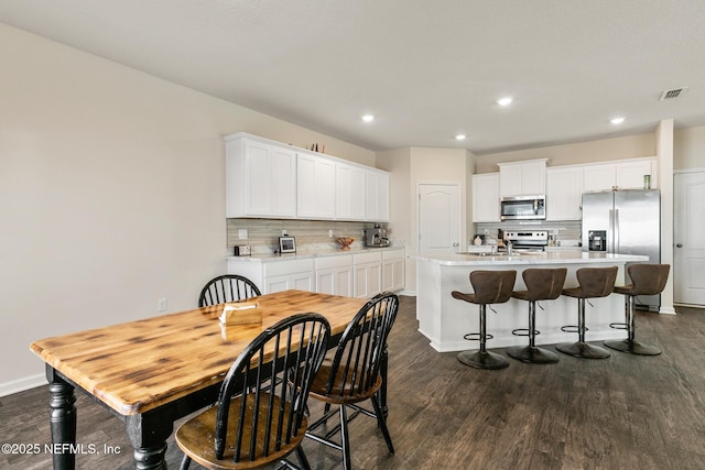 kitchen featuring white cabinetry, dark hardwood / wood-style floors, an island with sink, and appliances with stainless steel finishes