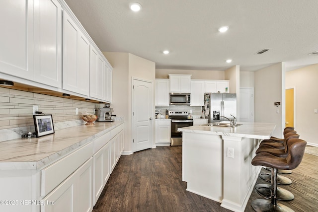 kitchen featuring white cabinetry, sink, a kitchen bar, stainless steel appliances, and a center island with sink