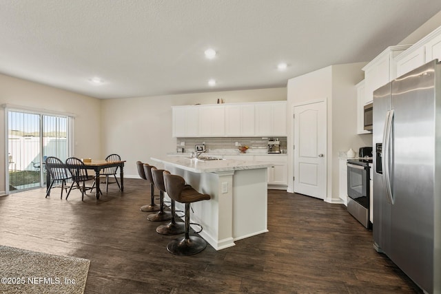 kitchen featuring stainless steel appliances, dark hardwood / wood-style floors, an island with sink, white cabinets, and decorative backsplash