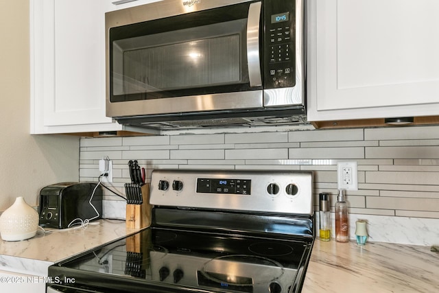 kitchen with stainless steel appliances, white cabinetry, light stone countertops, and tasteful backsplash