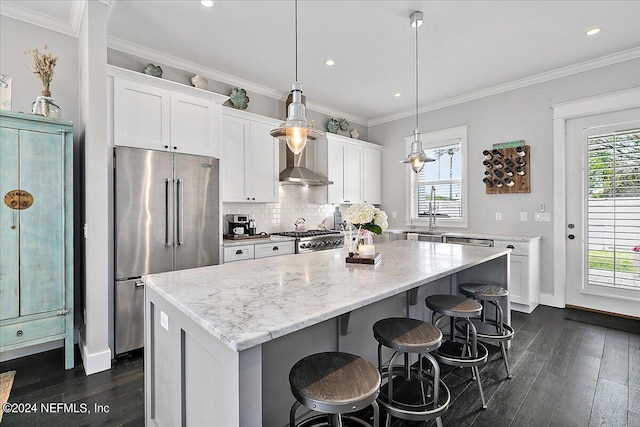 kitchen with a center island, a wealth of natural light, high end fridge, wall chimney range hood, and range