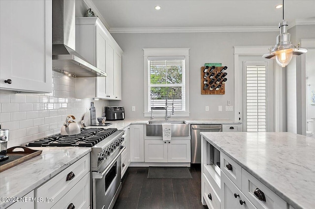 kitchen with crown molding, appliances with stainless steel finishes, white cabinets, a sink, and wall chimney exhaust hood