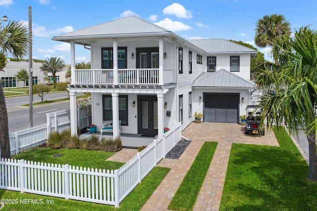 beach home featuring a porch, decorative driveway, a fenced front yard, and a front lawn