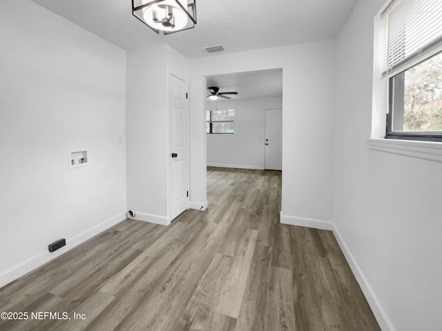 hall with an inviting chandelier, light hardwood / wood-style floors, a textured ceiling, and a wealth of natural light