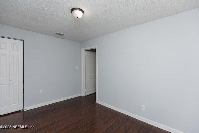 unfurnished bedroom featuring a textured ceiling, dark hardwood / wood-style flooring, and a closet