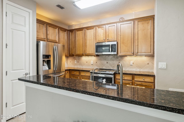 kitchen featuring dark stone countertops, decorative backsplash, stainless steel appliances, and kitchen peninsula