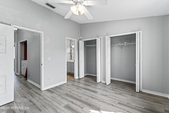 unfurnished bedroom featuring lofted ceiling, ensuite bath, light hardwood / wood-style flooring, two closets, and ceiling fan