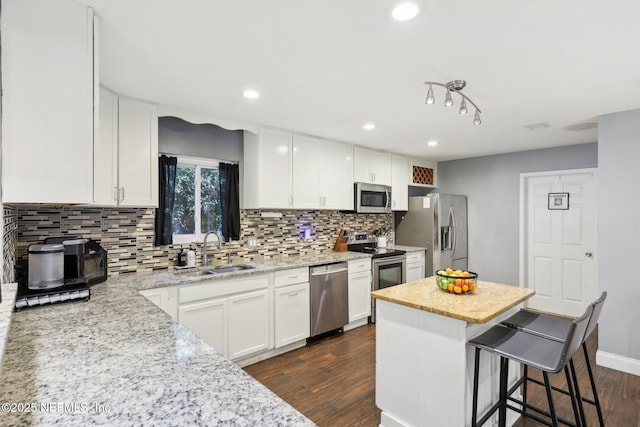 kitchen featuring a kitchen bar, sink, light stone counters, white cabinetry, and stainless steel appliances