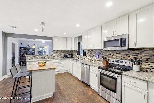 kitchen featuring white cabinetry, stainless steel appliances, light stone countertops, and a kitchen island