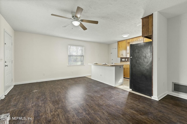 kitchen featuring a textured ceiling, black refrigerator, wood-type flooring, and kitchen peninsula