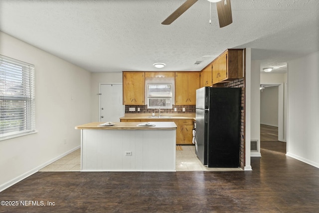 kitchen with backsplash, a center island, a textured ceiling, ceiling fan, and black refrigerator