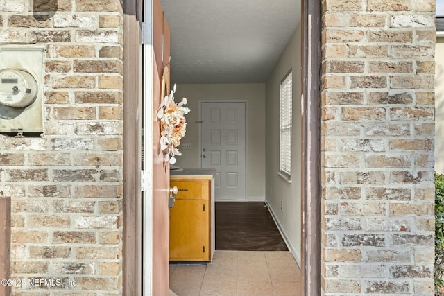 hall featuring light tile patterned floors, baseboards, and a textured ceiling