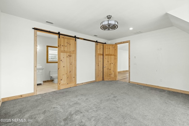 unfurnished bedroom featuring a barn door, visible vents, and light colored carpet