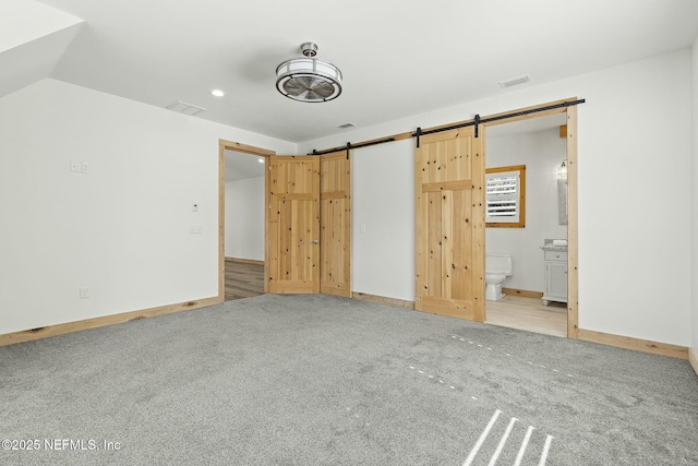 unfurnished bedroom featuring light carpet, a barn door, visible vents, and ensuite bathroom