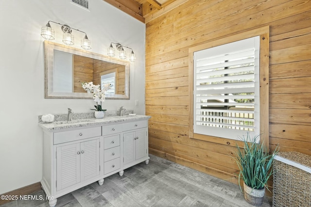 bathroom featuring double vanity, wood walls, a sink, and visible vents