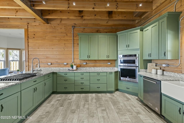 kitchen with stainless steel appliances, green cabinetry, and wood walls