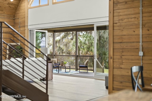 doorway featuring high vaulted ceiling, plenty of natural light, and wooden walls