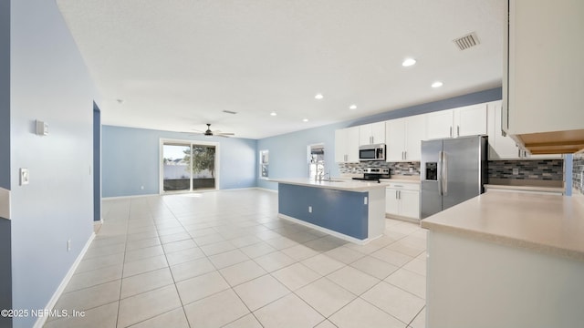 kitchen with stainless steel appliances, light countertops, white cabinets, and a center island with sink