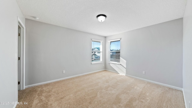 empty room featuring light carpet, a textured ceiling, and baseboards