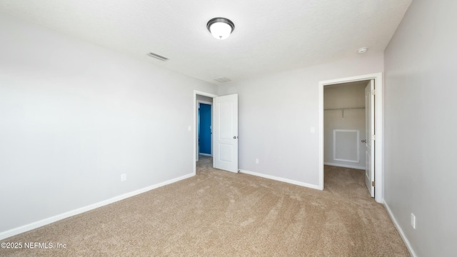 unfurnished bedroom with baseboards, visible vents, a walk in closet, and light colored carpet