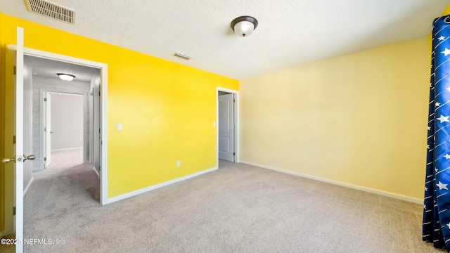 interior space with a textured ceiling, baseboards, visible vents, and light colored carpet