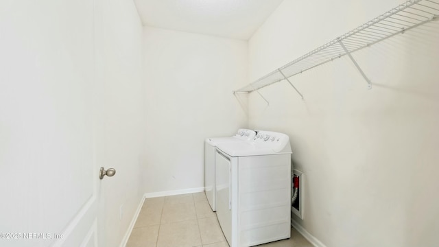 washroom with light tile patterned floors, laundry area, washer and clothes dryer, and baseboards