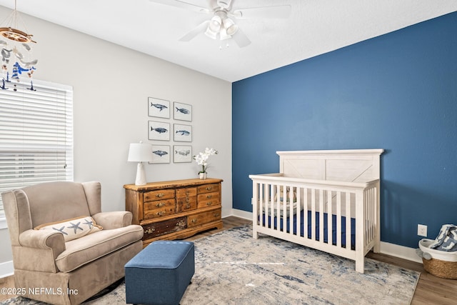 bedroom with a nursery area, hardwood / wood-style floors, and ceiling fan