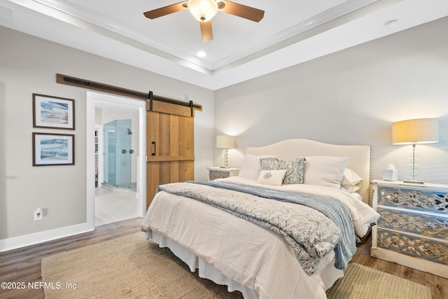 bedroom featuring crown molding, a barn door, wood-type flooring, and a tray ceiling