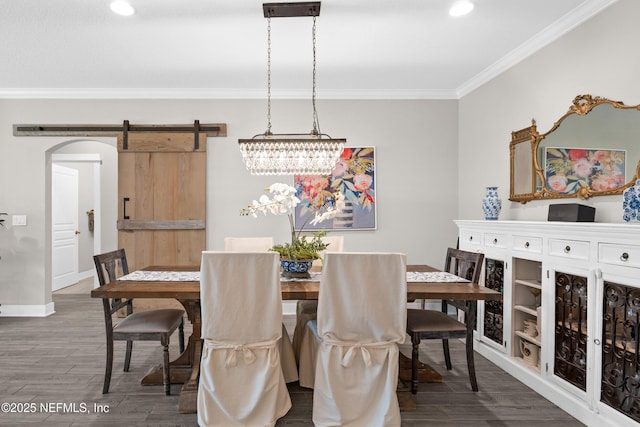 dining room featuring a barn door, ornamental molding, and dark hardwood / wood-style floors