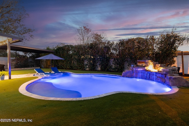 pool at dusk with a fire pit, a lawn, and pool water feature