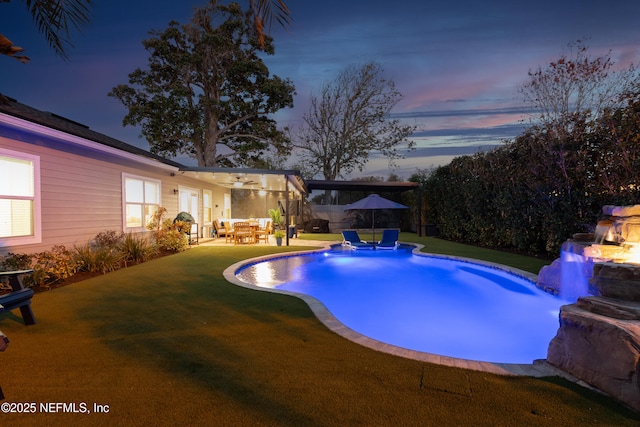 pool at dusk with a yard, ceiling fan, and a patio area