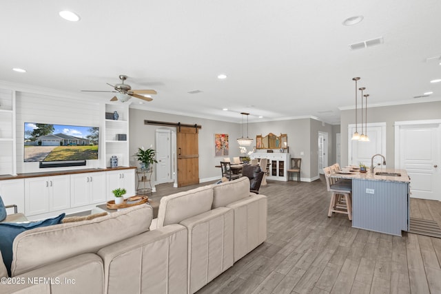 living room with ornamental molding, a barn door, light hardwood / wood-style floors, and sink