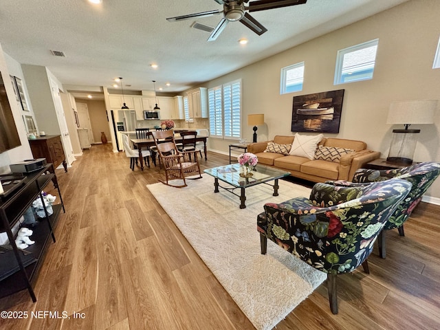 living room featuring ceiling fan, a textured ceiling, and light hardwood / wood-style flooring