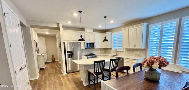 kitchen featuring a kitchen island, appliances with stainless steel finishes, white cabinets, hanging light fixtures, and light hardwood / wood-style flooring