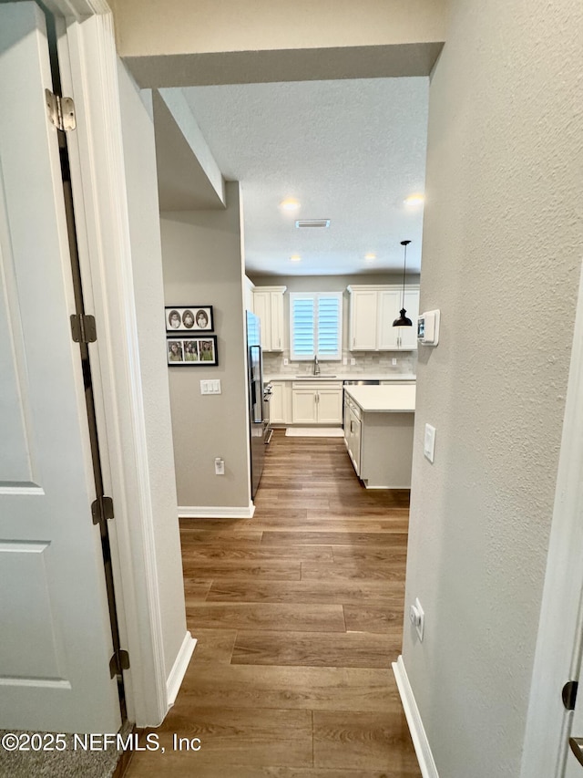 hallway with sink, a textured ceiling, and light wood-type flooring