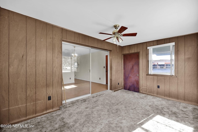 unfurnished bedroom with a closet, ceiling fan with notable chandelier, wood walls, and carpet flooring