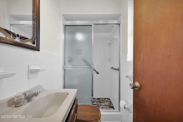 bathroom with vanity, toilet, a shower with shower door, and tile walls