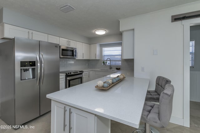 kitchen with sink, white cabinetry, a kitchen breakfast bar, stainless steel appliances, and decorative backsplash