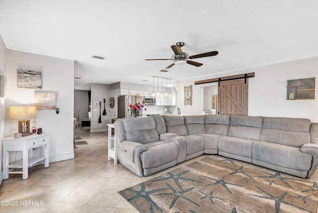 living area with a barn door, visible vents, baseboards, ceiling fan, and light tile patterned flooring