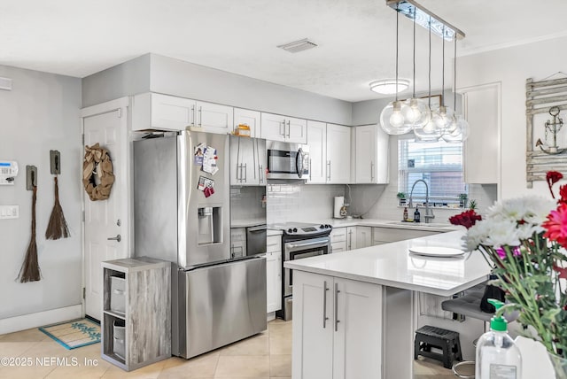 kitchen featuring appliances with stainless steel finishes, white cabinets, light countertops, and pendant lighting