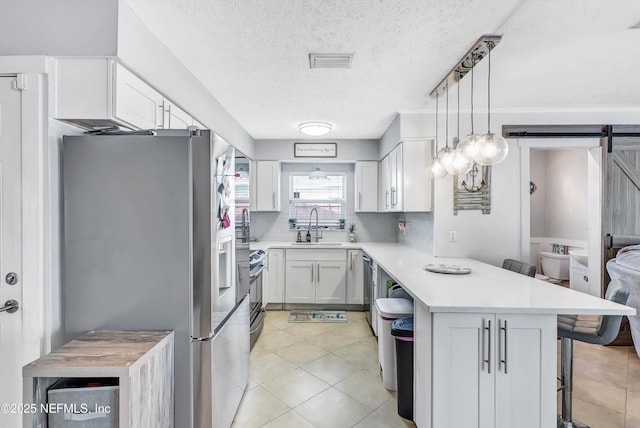 kitchen with stainless steel appliances, light countertops, a barn door, a peninsula, and a kitchen bar