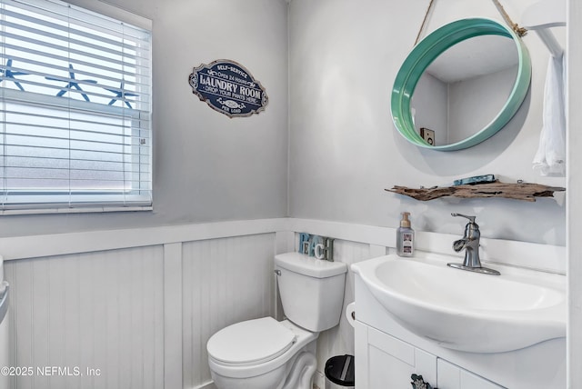 half bath featuring toilet, a wainscoted wall, and vanity