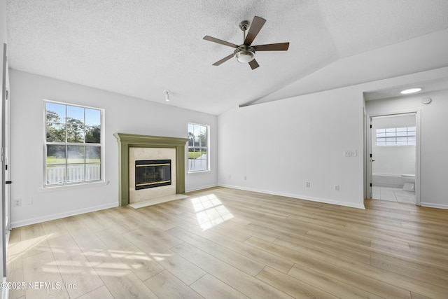 unfurnished living room featuring a fireplace, light hardwood / wood-style floors, vaulted ceiling, ceiling fan, and a textured ceiling