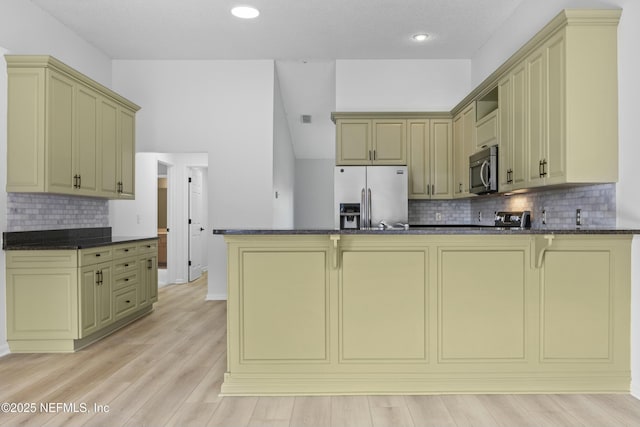 kitchen with kitchen peninsula, light hardwood / wood-style flooring, backsplash, dark stone counters, and appliances with stainless steel finishes