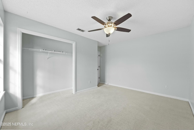 unfurnished bedroom featuring a textured ceiling, a closet, light carpet, and ceiling fan